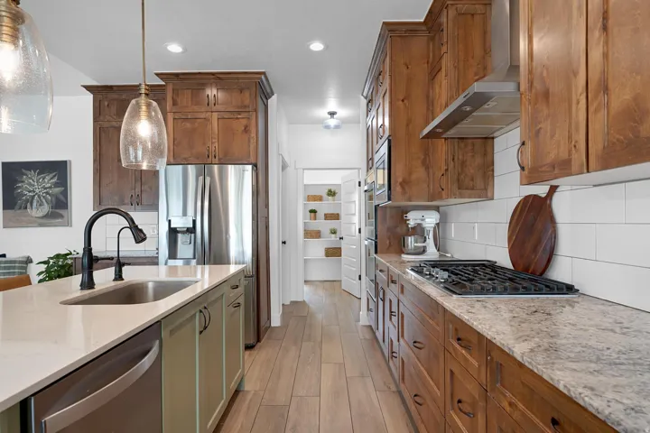 Kitchen featuring light stone countertops, hanging light fixtures, stainless steel appliances, wall chimney exhaust hood, and recessed lighting