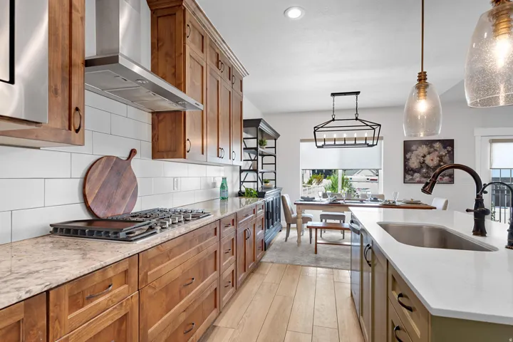 Kitchen featuring brown cabinets, light stone countertops, wall chimney exhaust hood, and recessed lighting