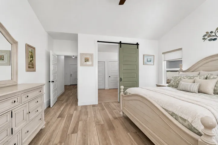 Spacious primary bedroom featuring hardwood flooring, a barn door with black hardware, dual built-in nightstands with drawer storage, and an ensuite bathroom