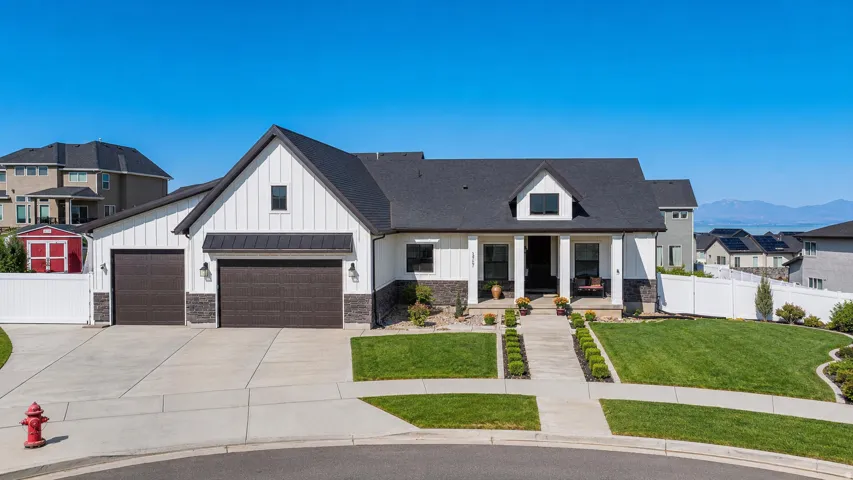 Contemporary farmhouse exterior with white vertical siding, dark gray stone accents, a deep porch, an attached two-car garage, and a concrete driveway