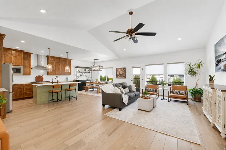 Vaulted ceiling with a ceiling fan, recessed lighting, wood-finish flooring, full kitchen with a center island and pendant lighting, and multiple windows