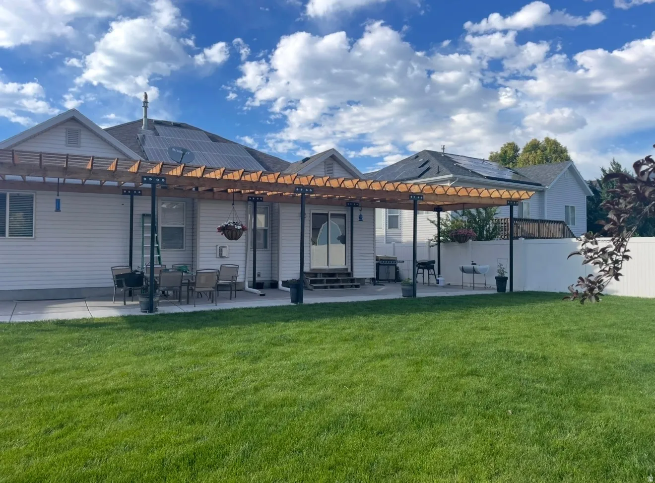 Expansive backyard featuring a lush lawn, white vinyl fencing, and a concrete patio with a wood pergola