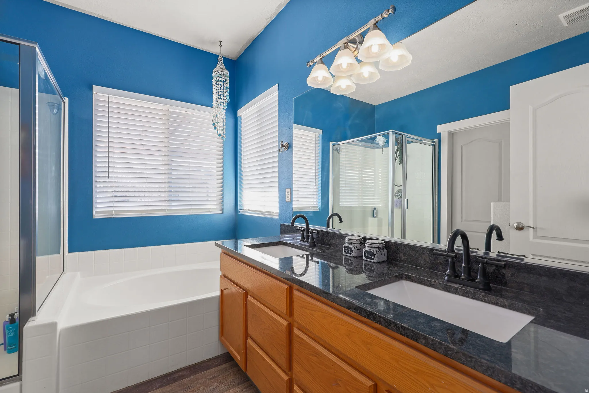 Bathroom with a bath, a stall shower, double vanity, dark wood finished floors, and a chandelier