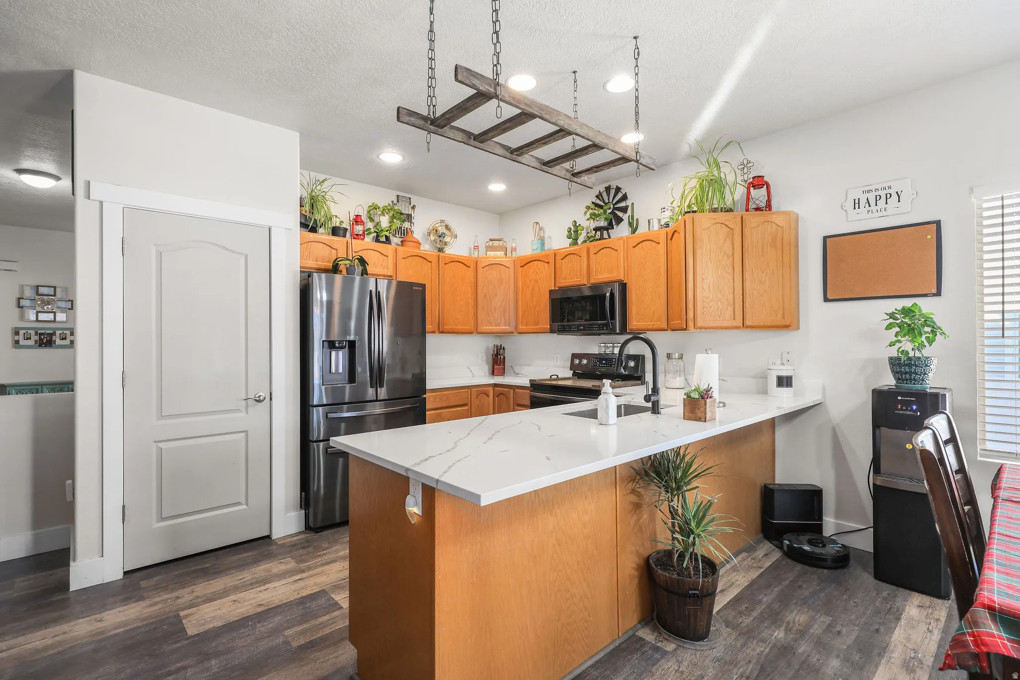 Kitchen with stainless steel appliances, dark wood-style floors, a peninsula, a textured ceiling, and light stone counters
