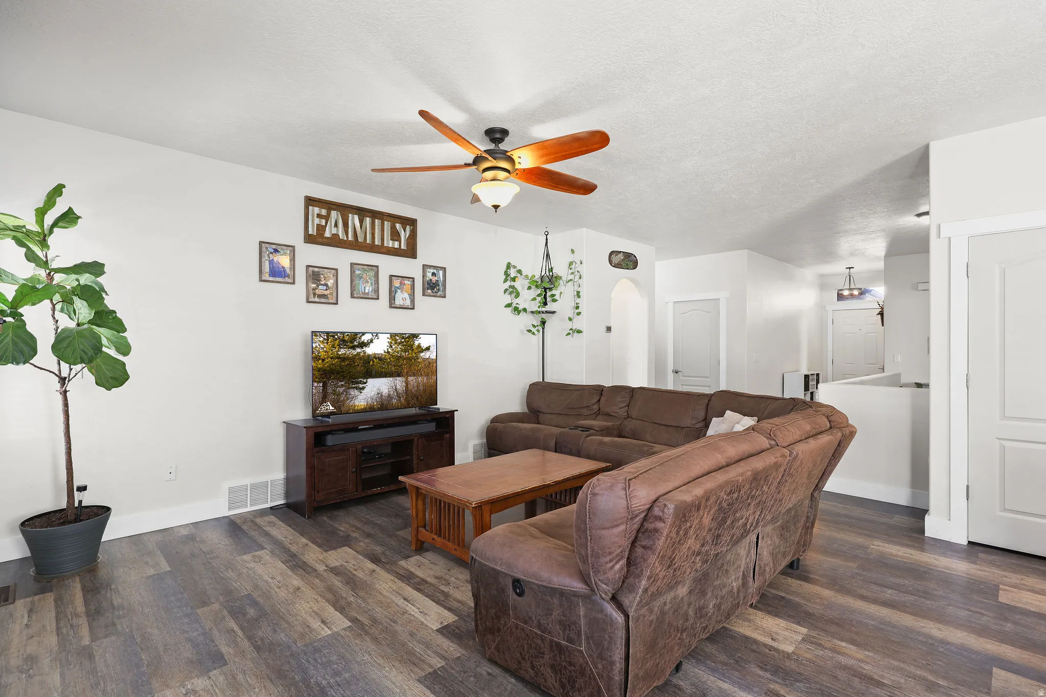 Living area featuring ceiling fan, dark wood-type flooring, a textured ceiling, and arched walkways