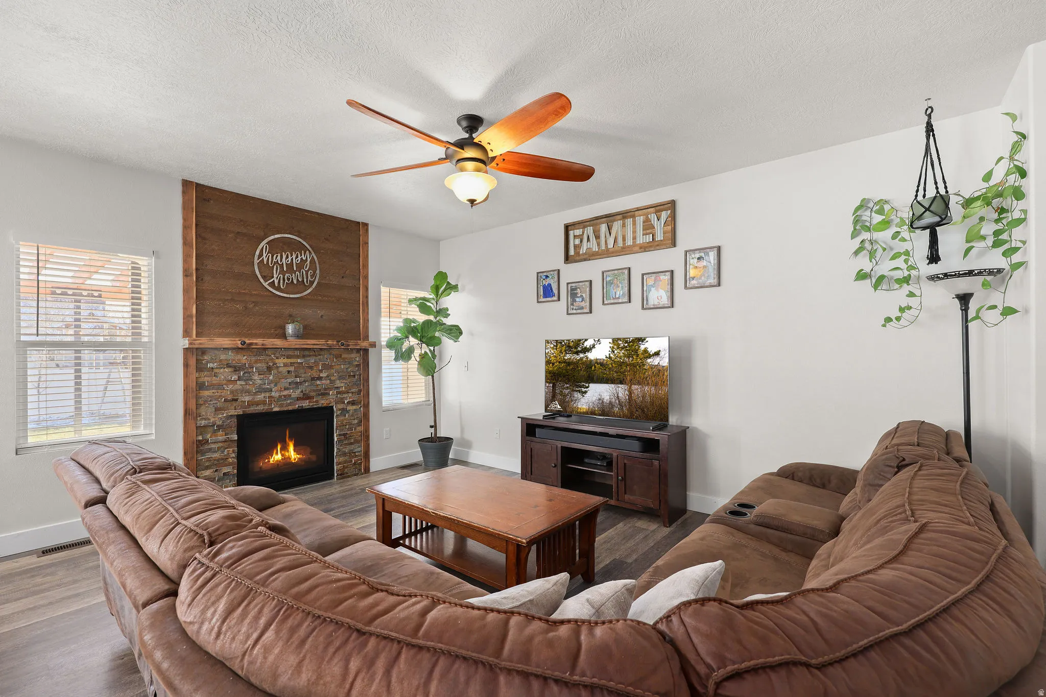 Living area with a stone fireplace, wood finished floors, ceiling fan, and a textured ceiling