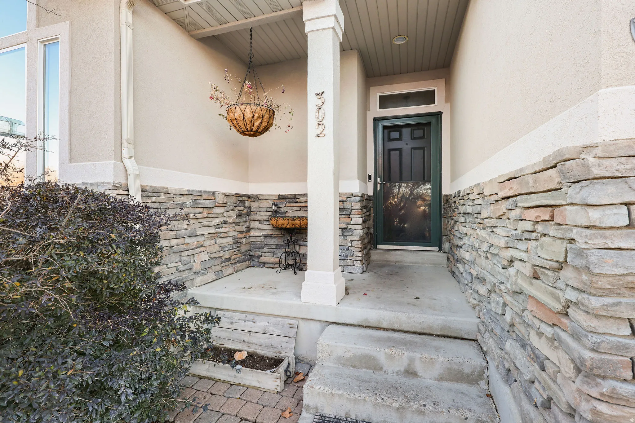 Doorway to property featuring stone siding, stucco siding, and covered porch