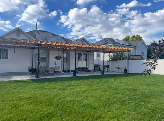 Expansive backyard featuring a lush lawn, white vinyl fencing, and a concrete patio with a wood pergola