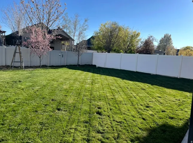 Expansive backyard featuring a lush lawn with distinct mow lines, surrounded by white privacy fencing