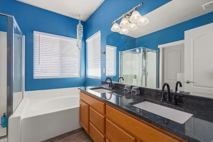 Bathroom with a bath, a stall shower, double vanity, dark wood finished floors, and a chandelier