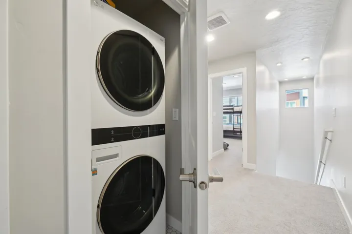 Laundry room featuring recessed lighting, estacked washer and dryer, and light carpet
