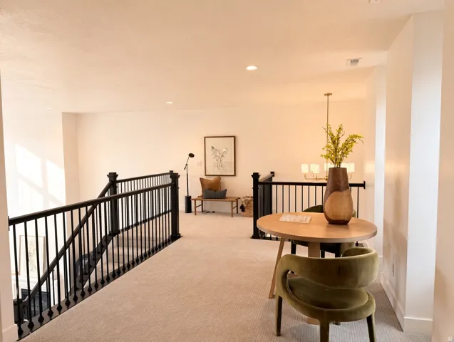 Open loft area featuring neutral carpeting, recessed lighting, and black metal railings
