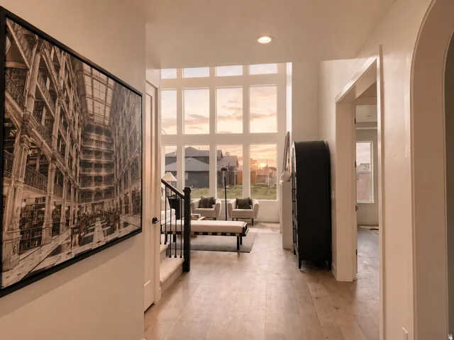 Expansive window wall, high ceilings, wood-finish flooring, staircase with black metal balusters, and an arched doorway