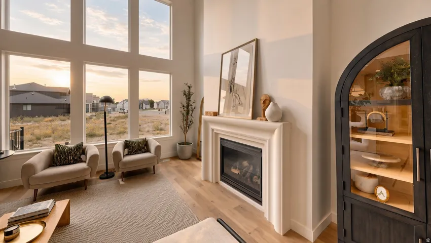 Two-story living area with expansive floor-to-ceiling windows, a built-in fireplace with a stone-finish mantel, and light wood-finish flooring
