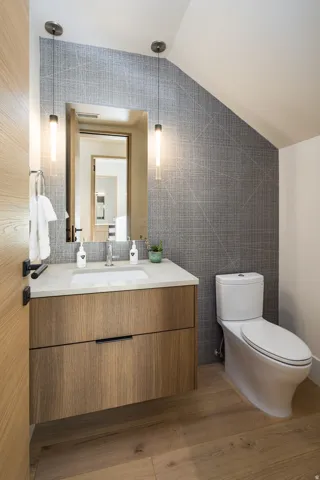 Half bath with tile walls, vanity, lofted ceiling, and dark wood-type flooring