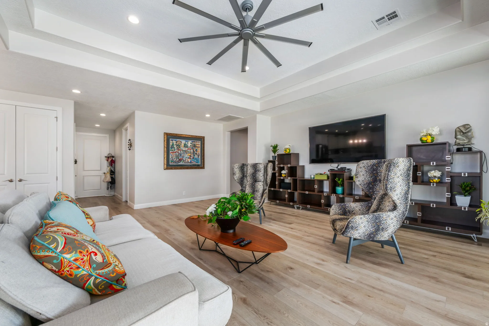 Living room with a raised ceiling, wood finished floors, ceiling fan, and recessed lighting