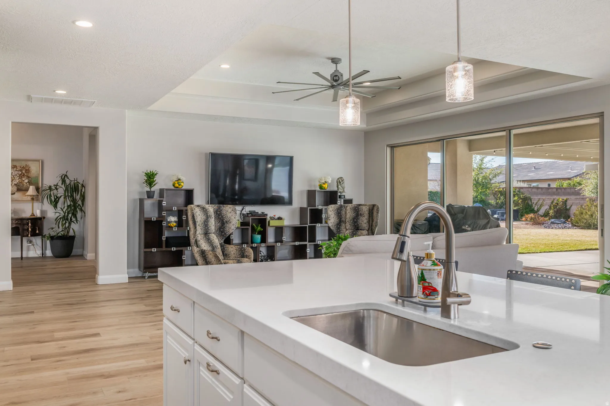Kitchen with a raised ceiling, a ceiling fan, white cabinetry, light stone counters, and open floor plan