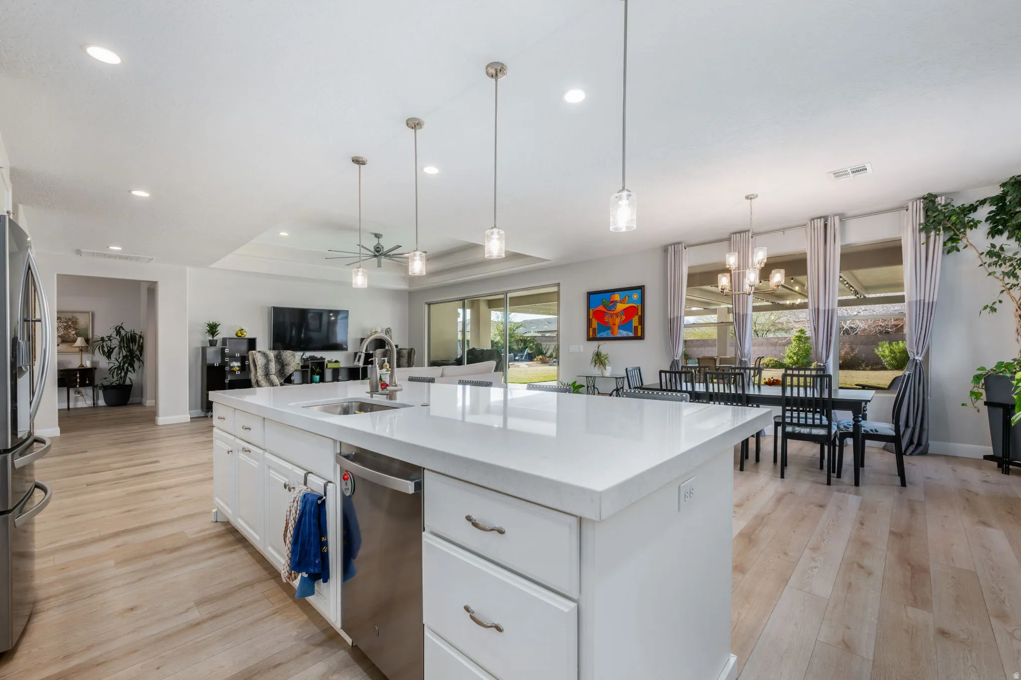 Kitchen featuring white cabinets, a center island with sink, open floor plan, light wood-style flooring, and decorative light fixtures