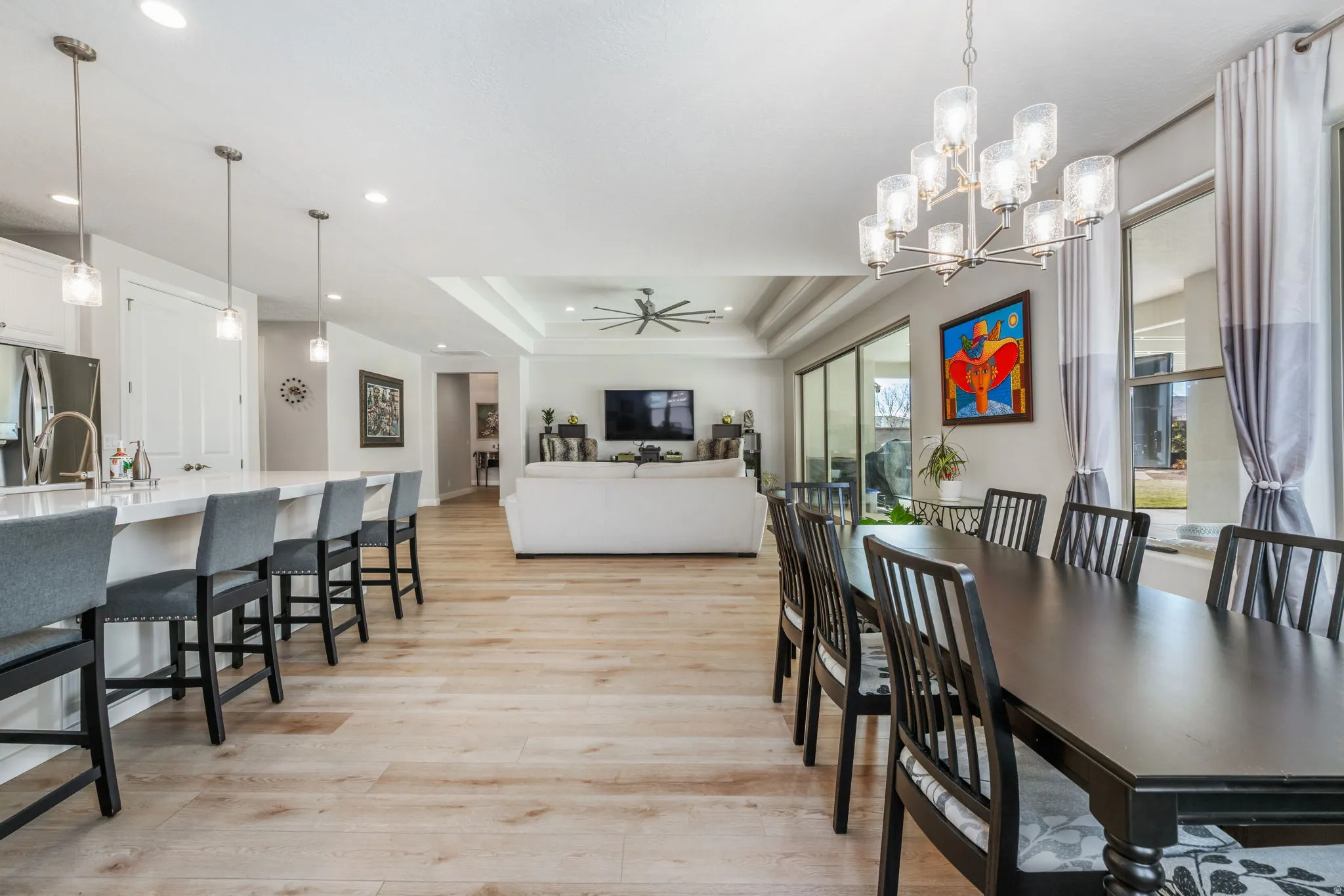 Dining space featuring a tray ceiling, light wood-style floors, ceiling fan, a chandelier, and recessed lighting