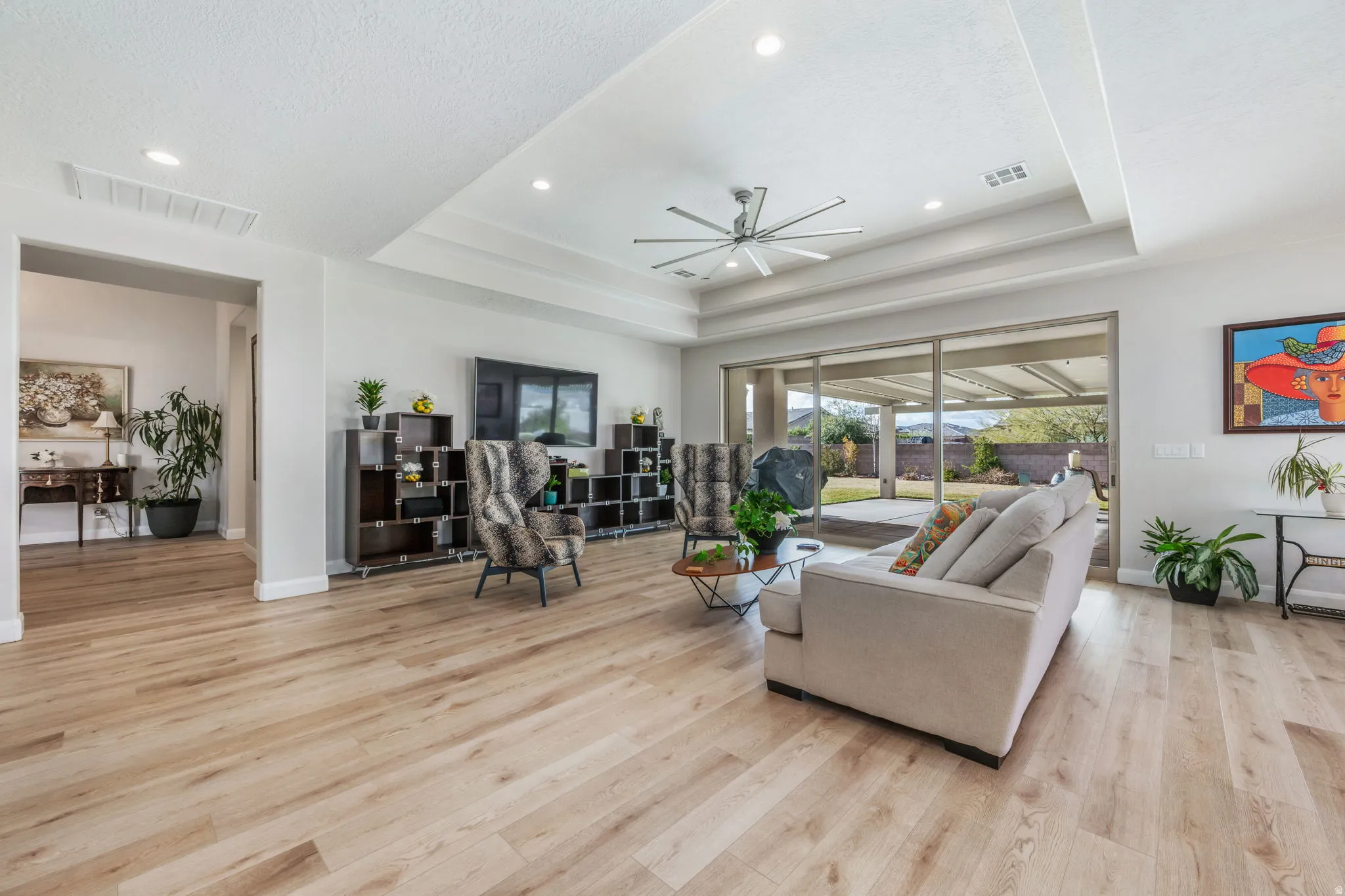 Living room with ceiling fan, light wood finished floors, a tray ceiling, and recessed lighting
