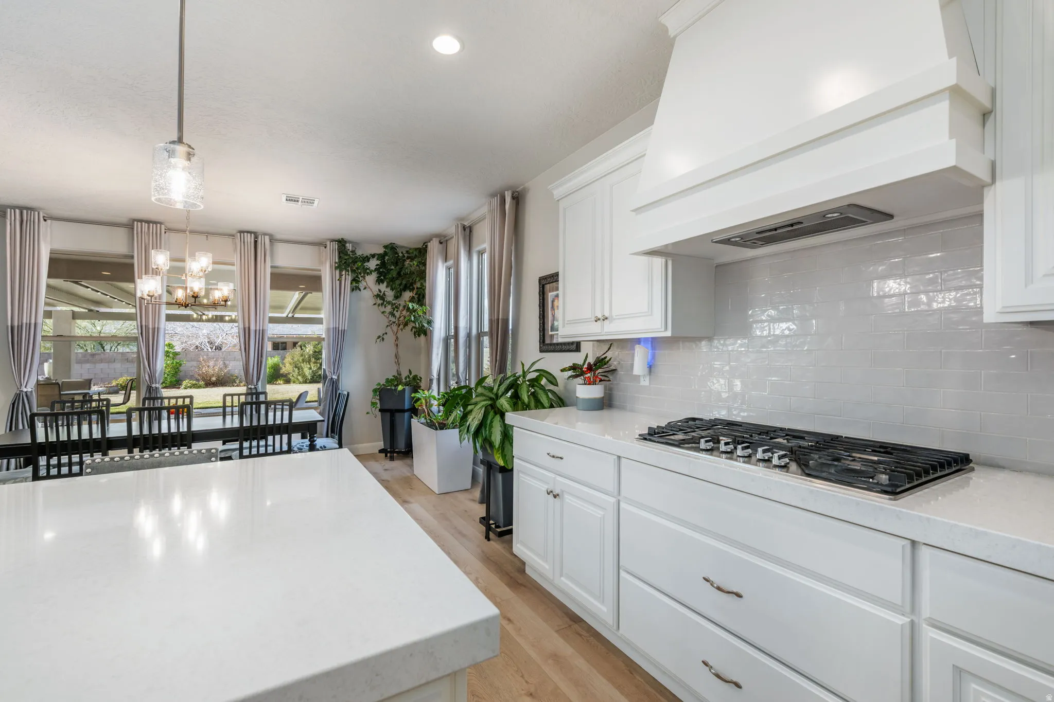 Kitchen featuring custom exhaust hood, hanging light fixtures, white cabinets, light stone counters, and light wood-type flooring