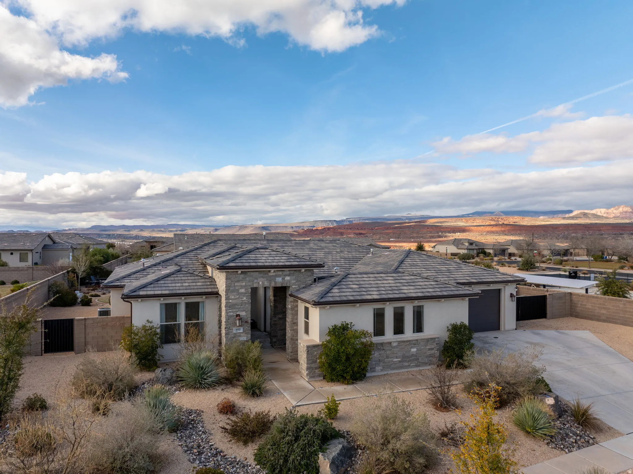 View of front of house featuring stucco siding, stone siding, concrete driveway, a gate, and an attached garage