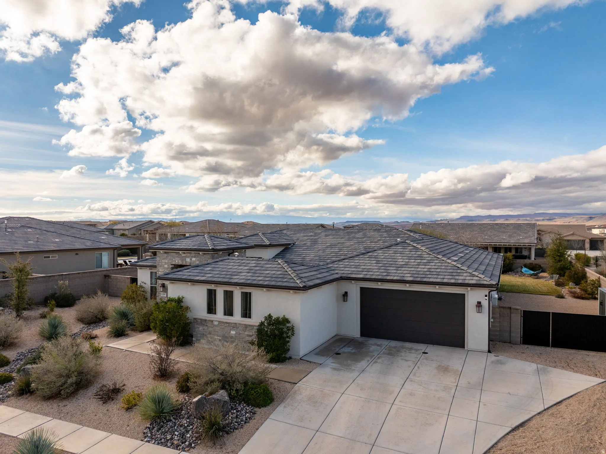 View of front of house with stucco siding, a garage, stone siding, driveway, and a residential view