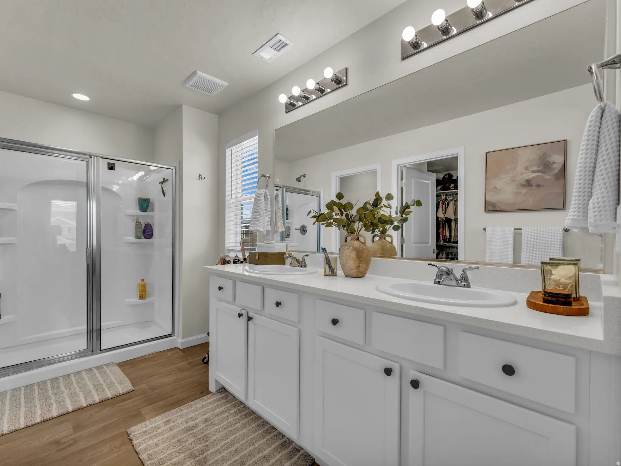 Bathroom with double vanity, a stall shower, a walk in closet, and light wood finished floors