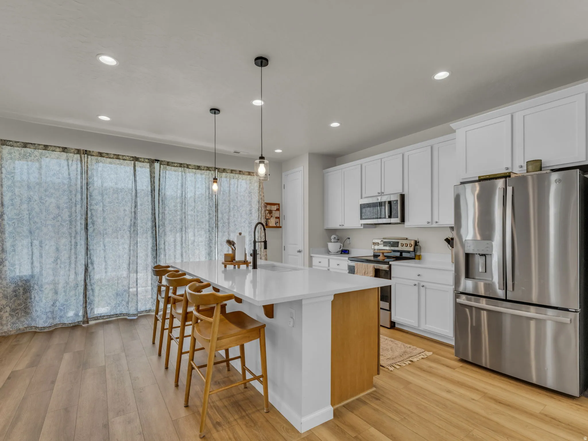 Kitchen with appliances with stainless steel finishes, white cabinetry, a kitchen breakfast bar, pendant lighting, and a center island with sink