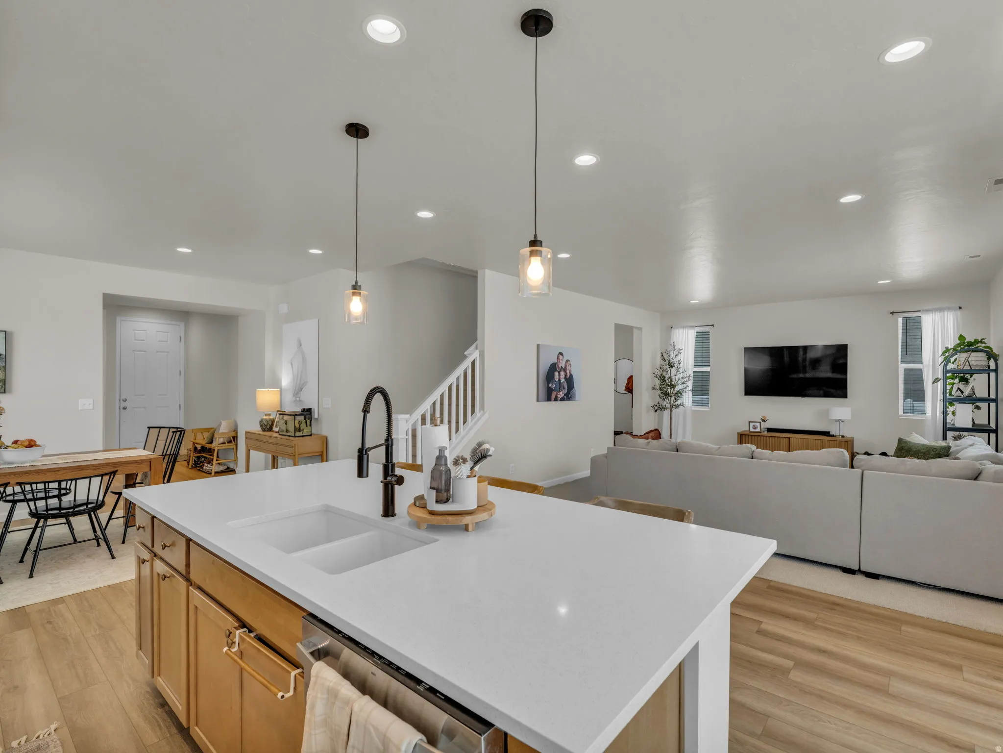 Kitchen with open floor plan, a kitchen island with sink, light wood-type flooring, stainless steel dishwasher, and hanging light fixtures