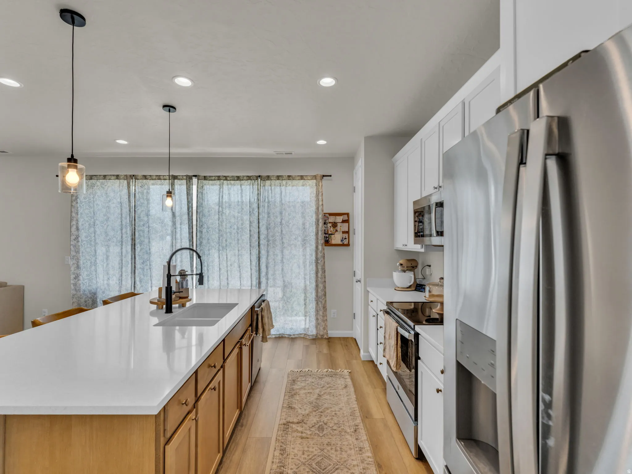 Kitchen featuring appliances with stainless steel finishes, white cabinets, decorative light fixtures, an island with sink, and light wood-style floors