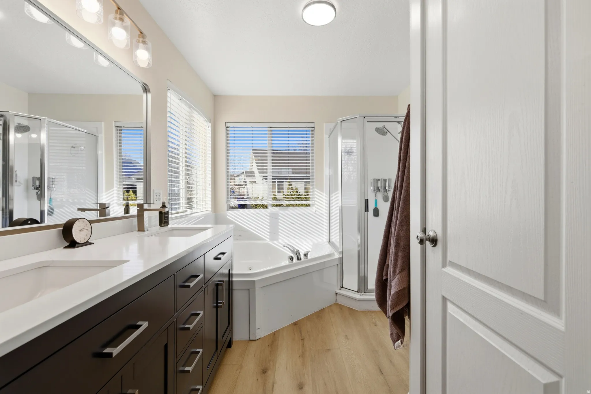 Full bath with double vanity, a stall shower, a tub with jets, and light wood-type flooring