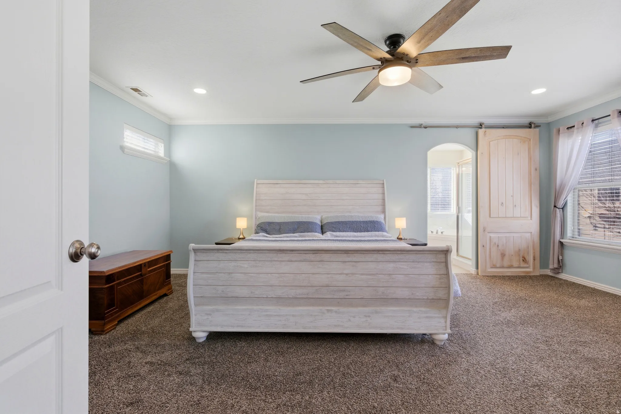 Carpeted bedroom featuring ornamental molding, a ceiling fan, a barn door, arched walkways, and recessed lighting