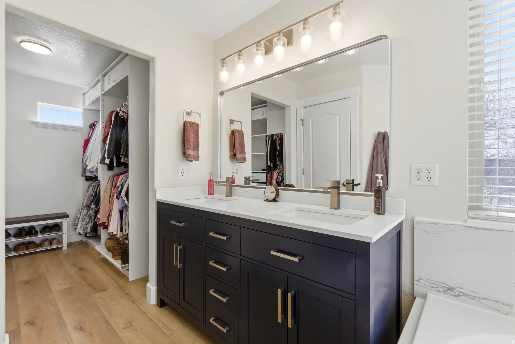 Full bath featuring a walk in closet, double vanity, light wood-style flooring, and a textured ceiling