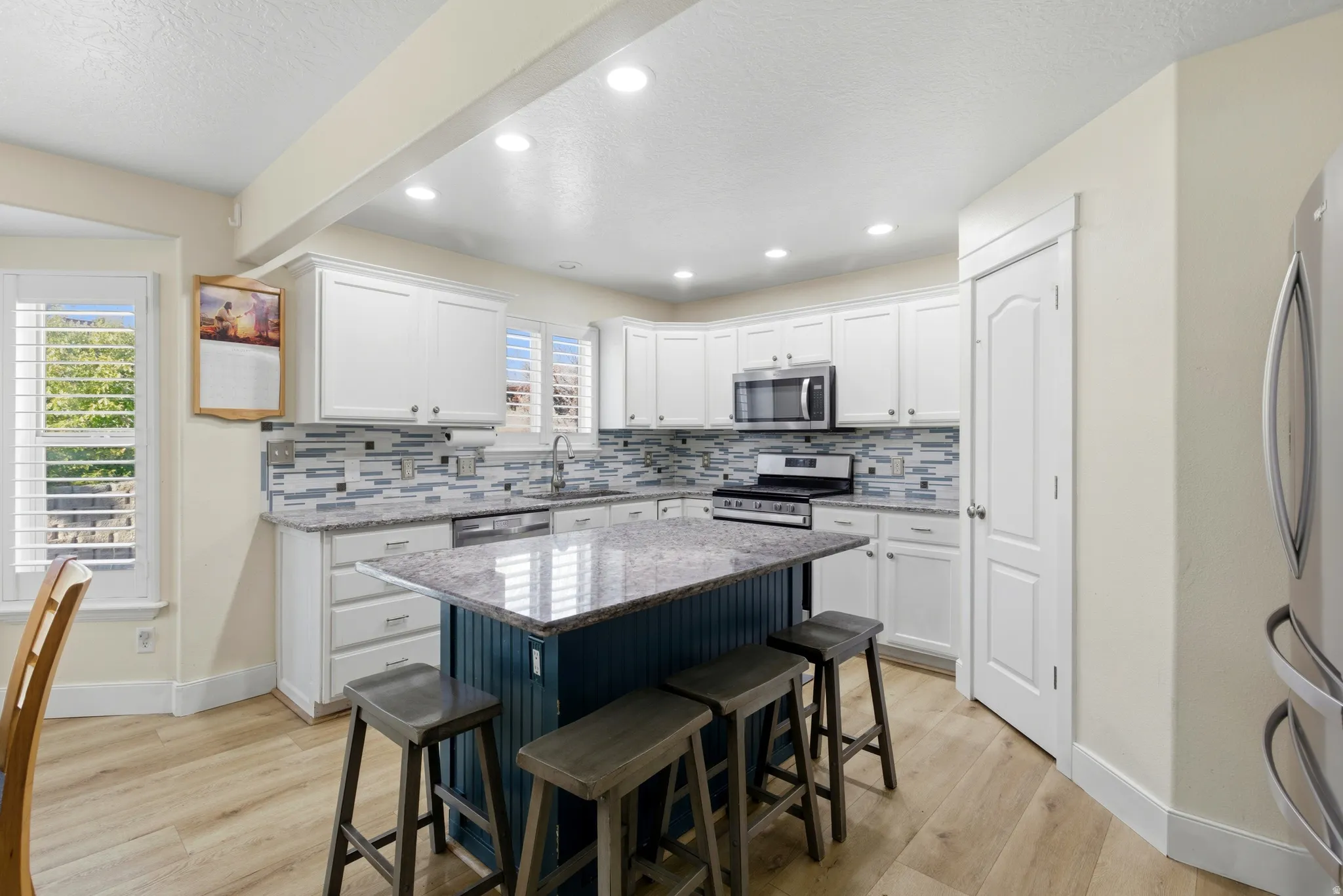 Kitchen featuring white cabinets, a kitchen bar, light stone counters, tasteful backsplash, and a textured ceiling