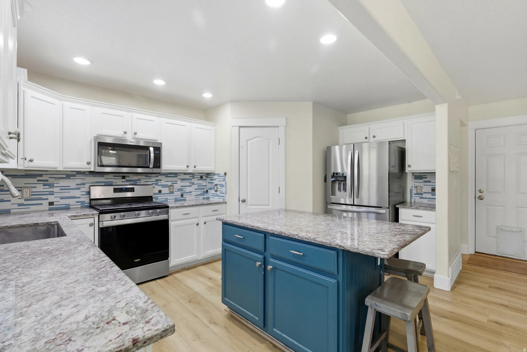 Kitchen with stainless steel appliances, white cabinetry, a kitchen island, blue cabinetry, and tasteful backsplash
