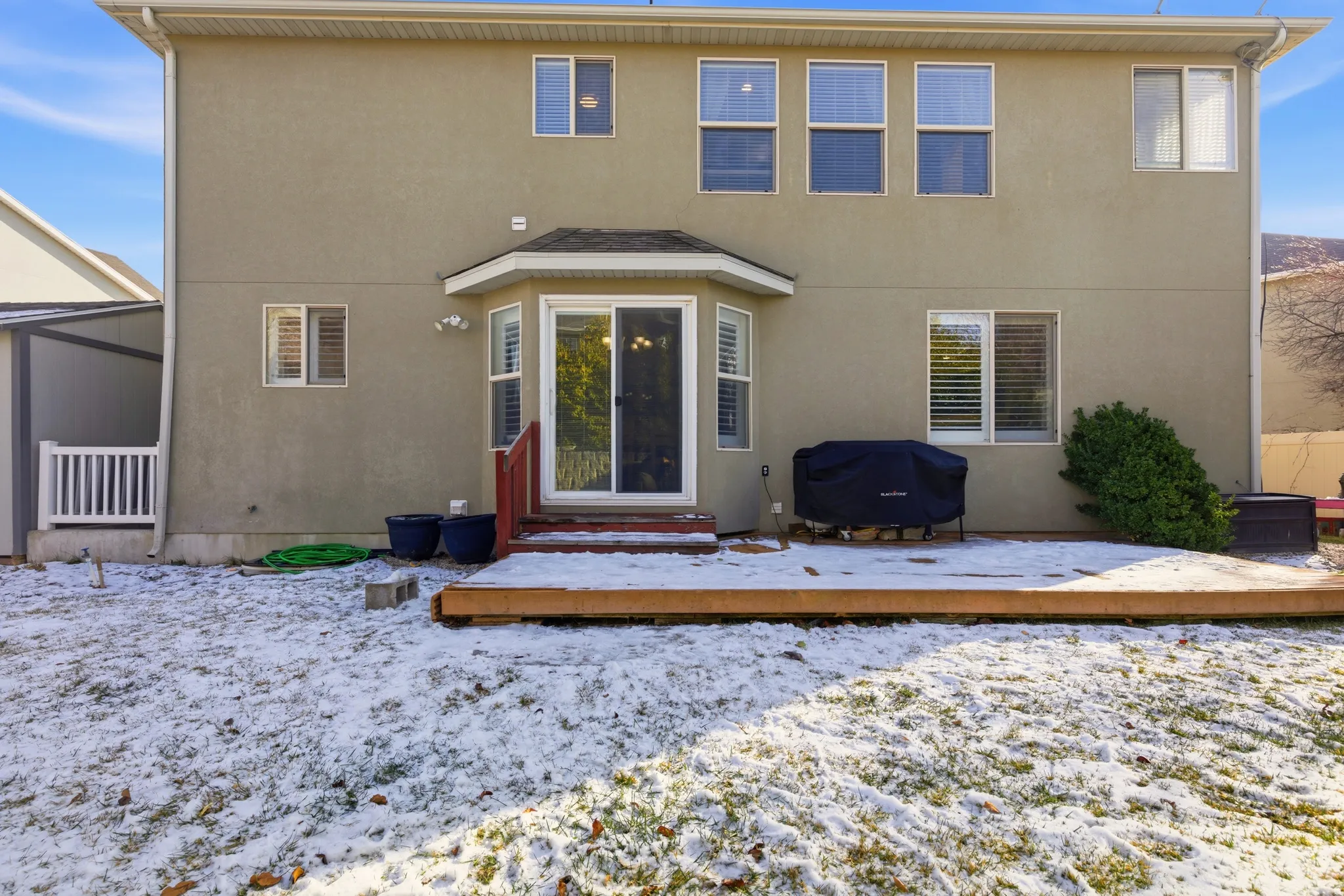 Snow covered rear of property featuring stucco siding, a deck, and entry steps