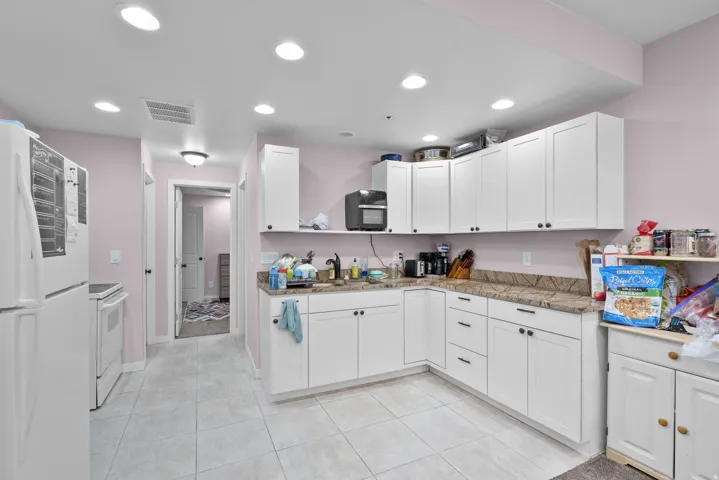 Kitchen featuring white appliances, white cabinets, light tile patterned floors, light stone counters, and recessed lighting