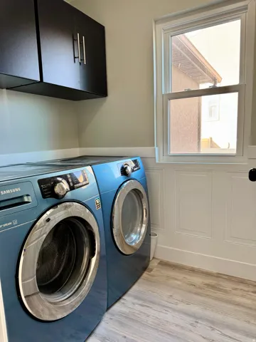 Laundry area with cabinet space, light wood finished floors, washer and clothes dryer, and wainscoting