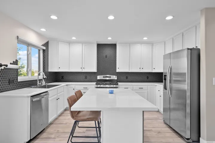 Kitchen with white cabinetry, stainless steel appliances, a breakfast bar area, light stone counters, and recessed lighting