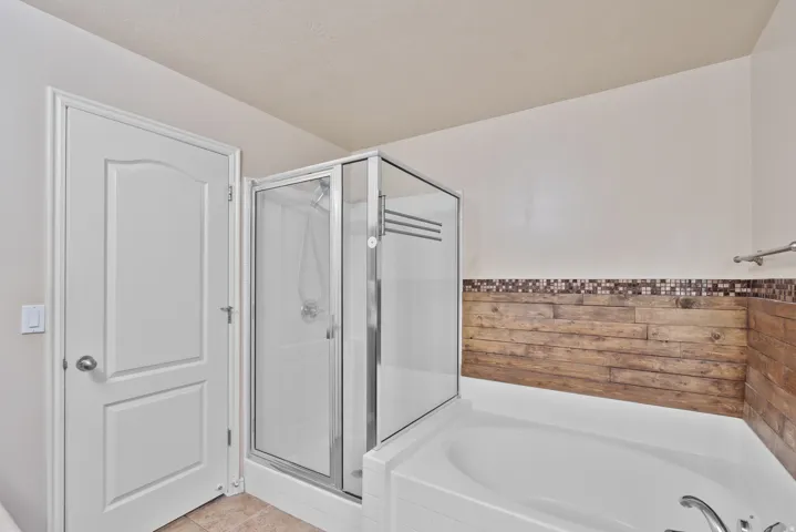Owners/Master Bathroom featuring a garden tub, a shower stall, light tile patterned flooring, and a wainscoted wall