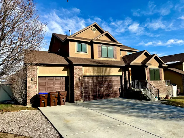 View of front of home with stucco siding, a shingled roof, concrete driveway, an attached garage, and brick siding
