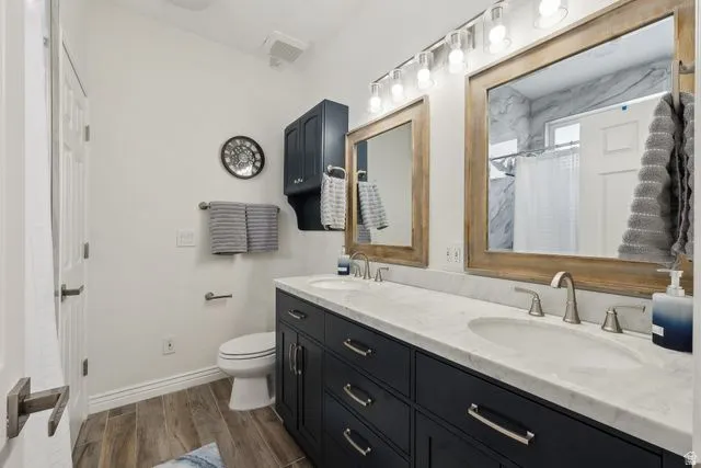 Bathroom with double vanity, curtained shower, and dark wood-style floors