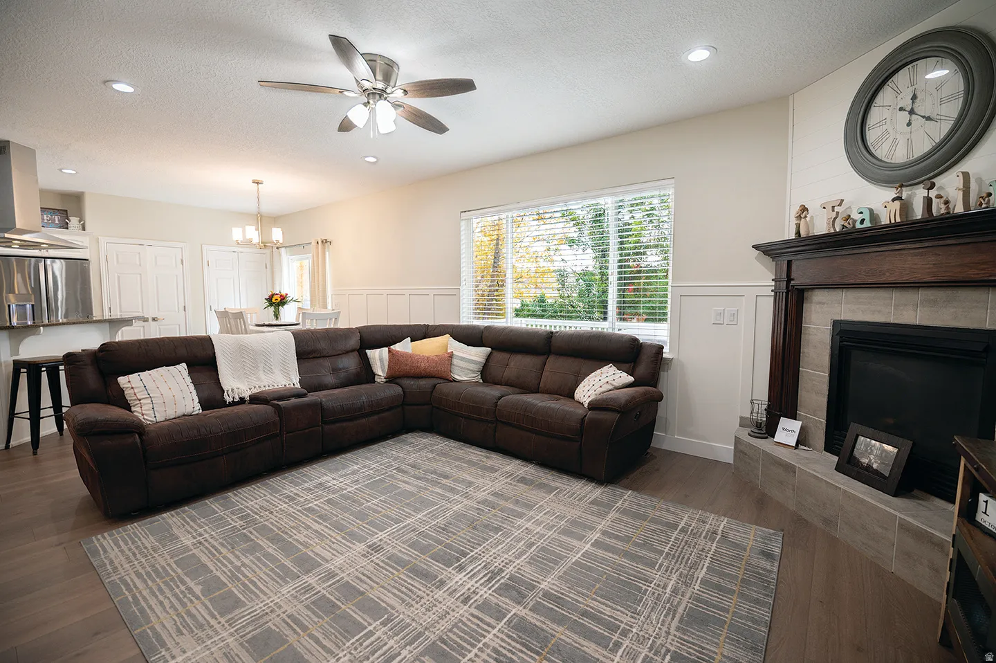Living area with a textured ceiling, dark wood-type flooring, ceiling fan, a tile fireplace, and wainscoting