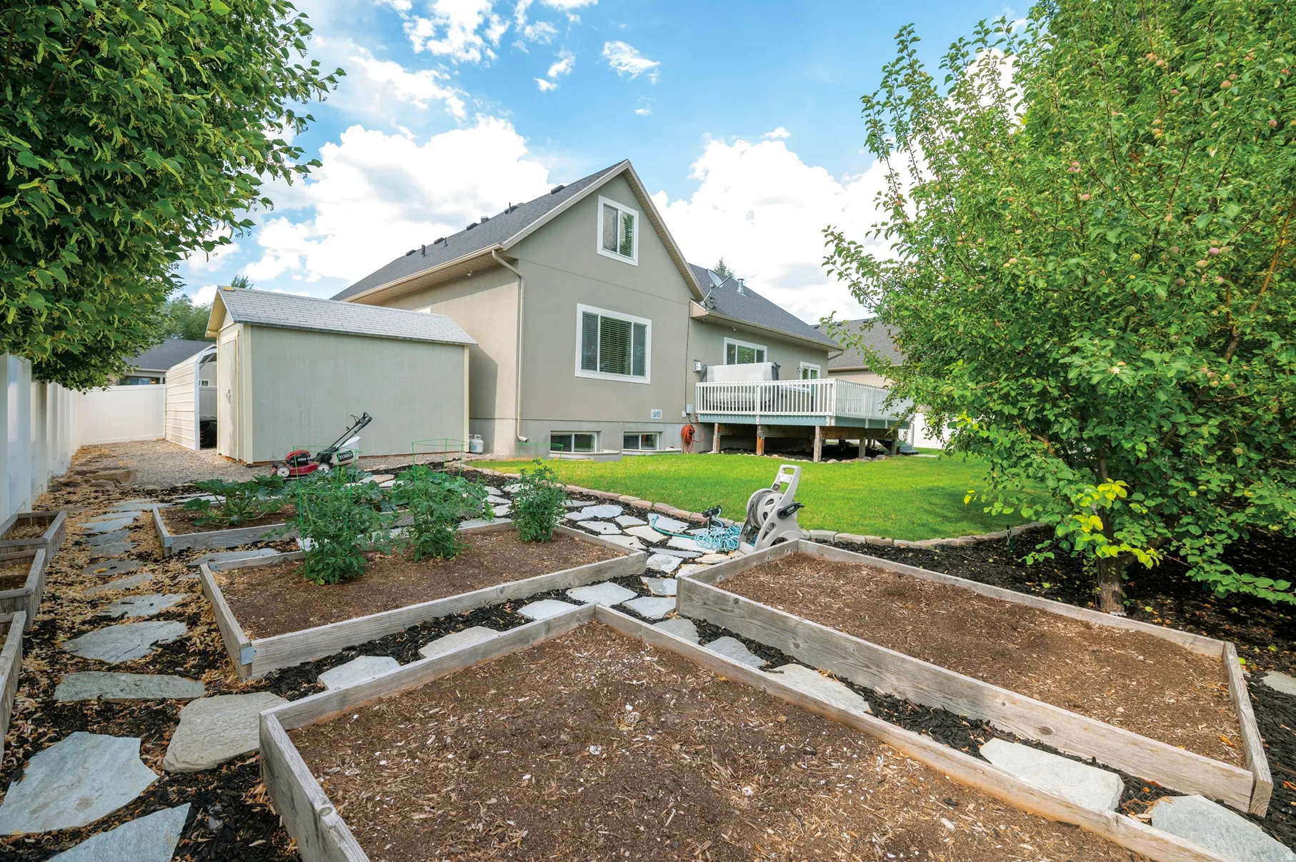 Rear view of property featuring stucco siding, a lawn, a vegetable garden, a wooden deck, and an outbuilding