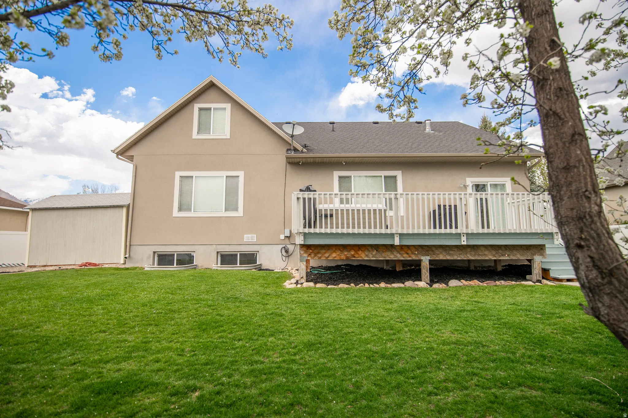 Back of house featuring stucco siding, a wooden deck, a yard, and a shingled roof