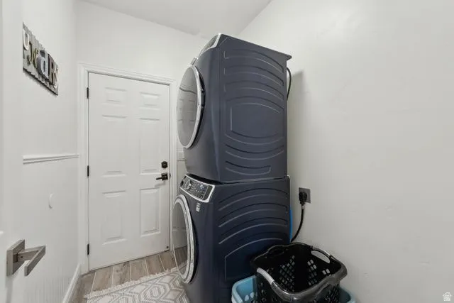 Washroom with stacked washer / dryer and light wood-style floors