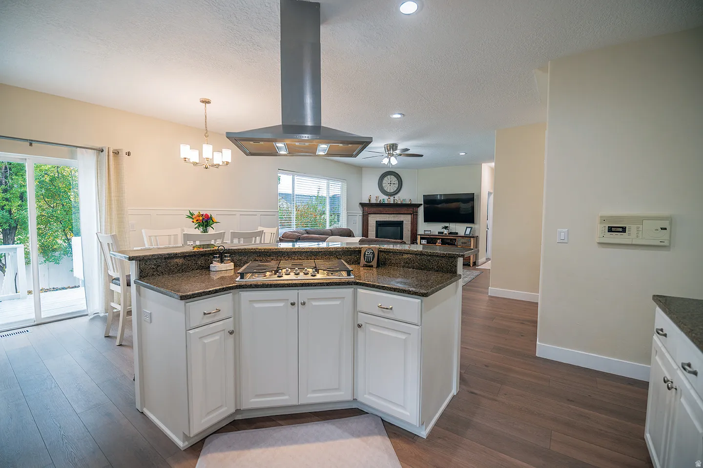 Kitchen featuring white cabinets, ventilation hood, a fireplace, dark wood-style floors, and a textured ceiling
