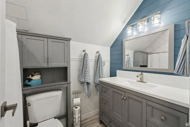Bathroom featuring vaulted ceiling, wood walls, a shower with shower curtain, and vanity