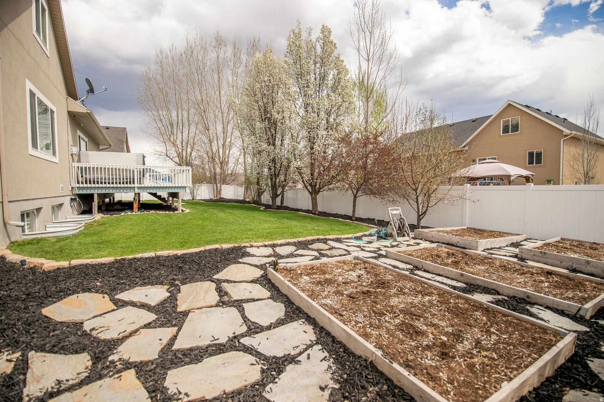 Fenced backyard featuring a vegetable garden, a deck, and a patio area